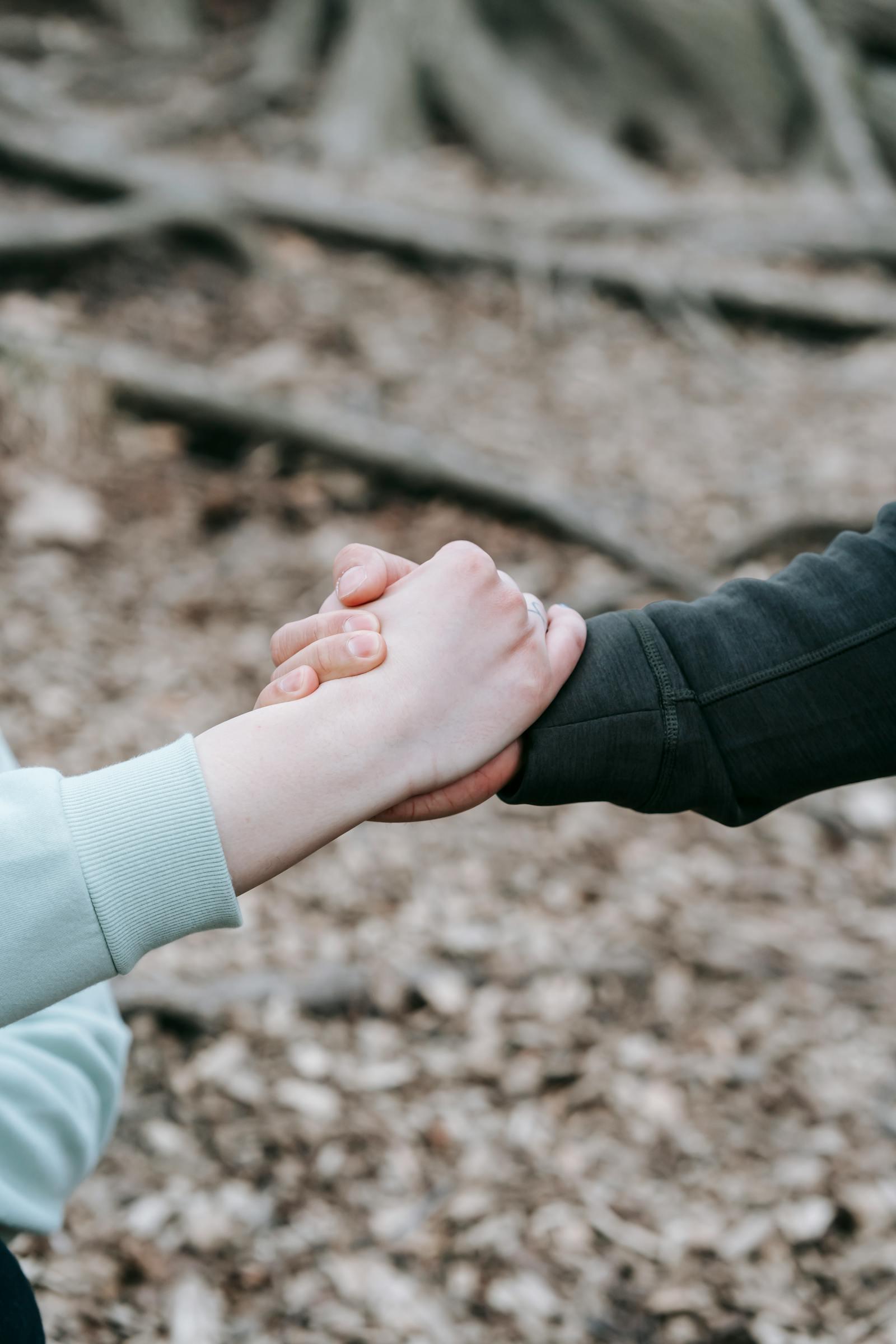 Two people clasping hands in a supportive moment outdoors.