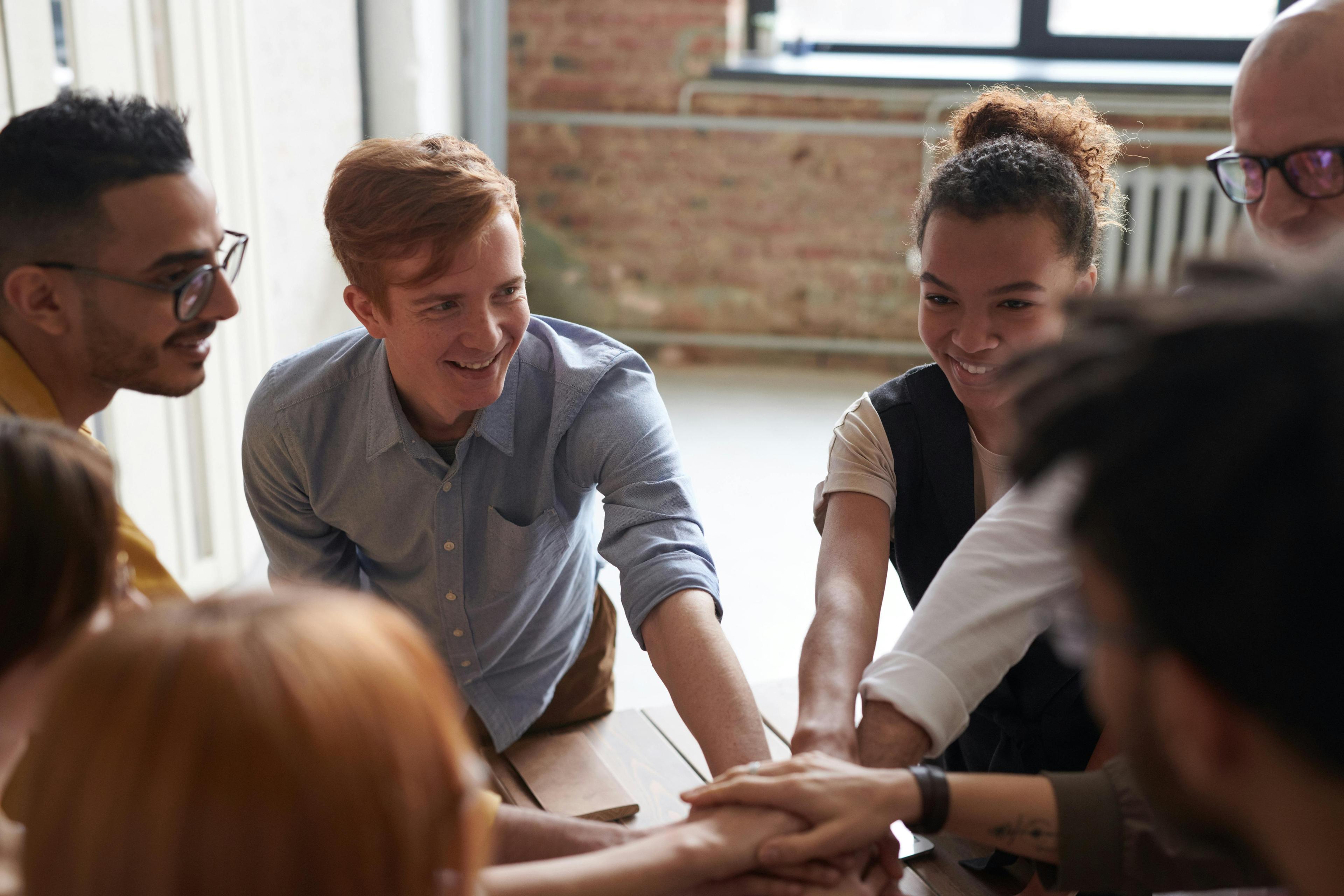 A team of social care workers leaning in around a table with hands stacked in the centre.