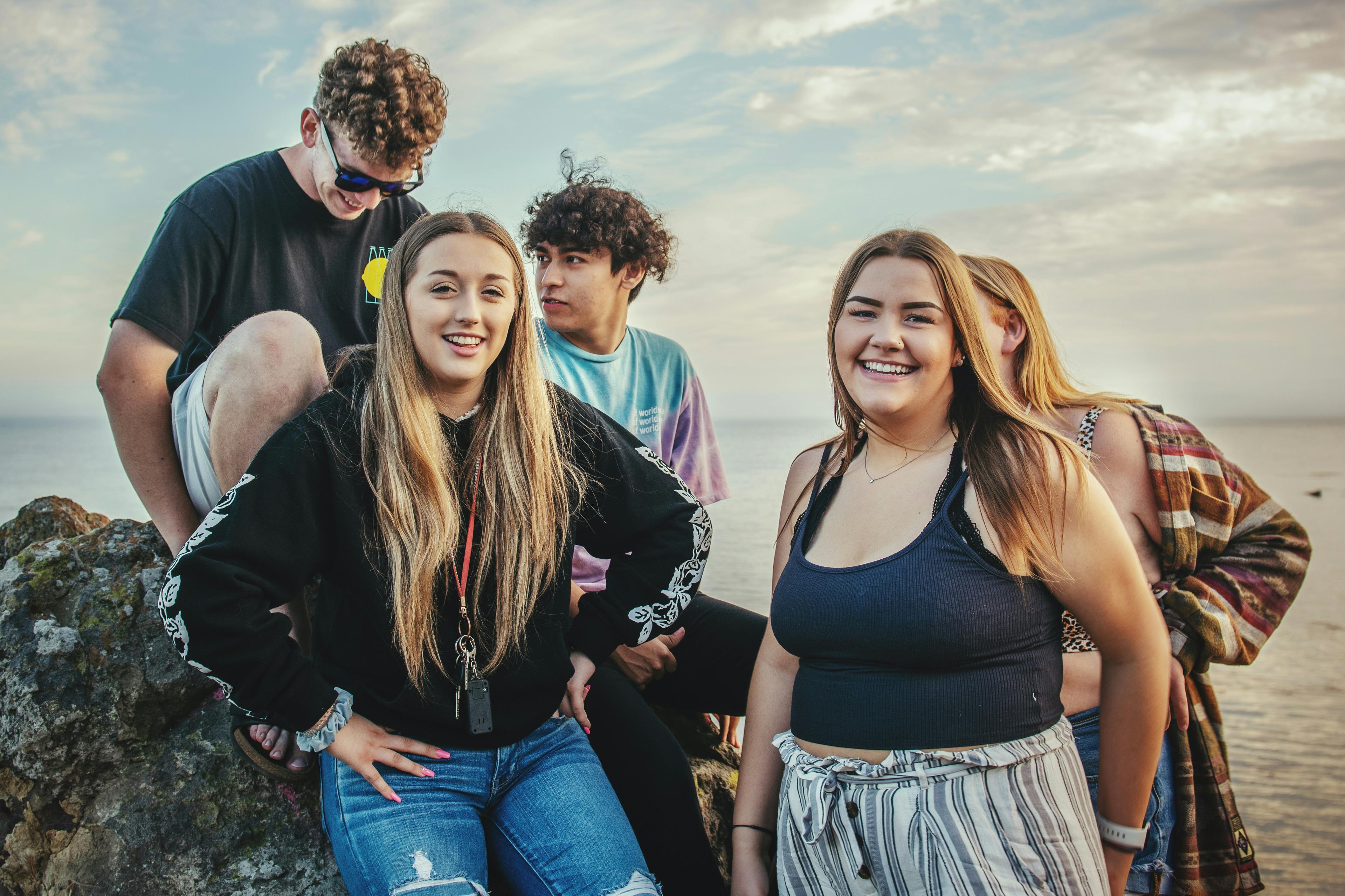 A group of young people gathered together on coastal rocks at golden hour.